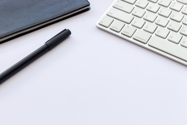 Livro, caneta e teclado de computador na mesa branca