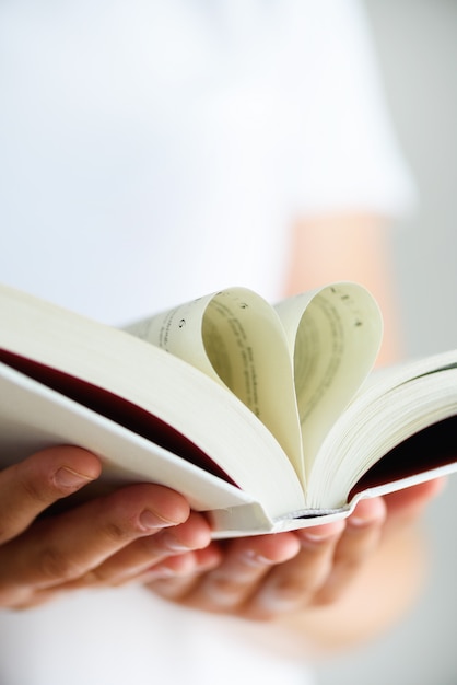 Livro com páginas abertas e forma de coração nas mãos da garota.