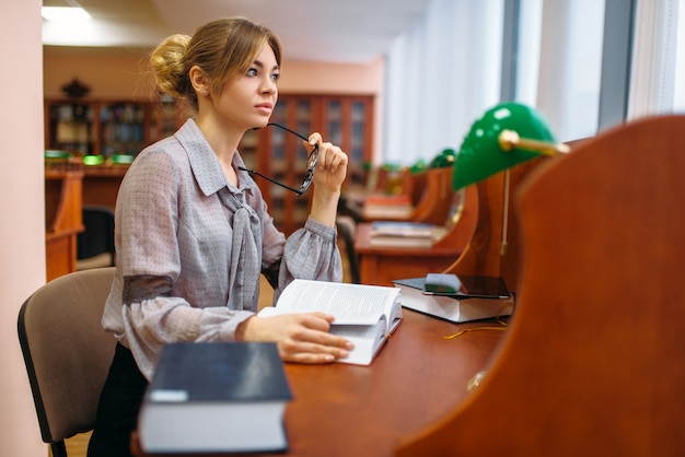 Livro de aprendizagem da aluna na biblioteca da universidade. Mulher estudando em depósito de conhecimento, educação