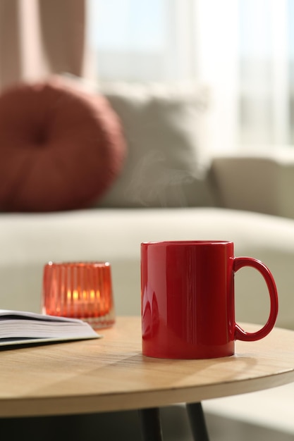 Livro de caneca vermelha e vela acesa na mesa de madeira dentro de casa Mockup para design