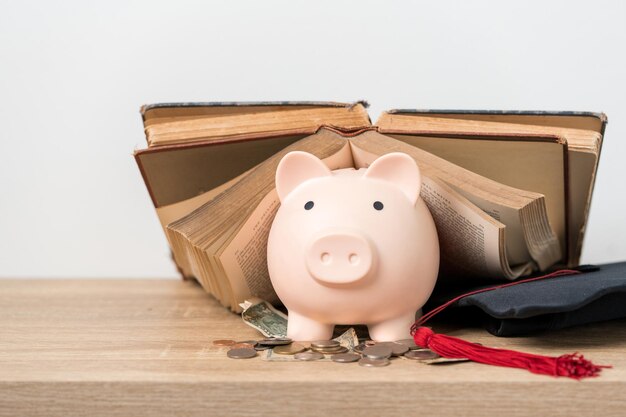 Livro de chapéu de formatura preto e investimento de conceito de cofrinho em educação Graduação economiza dinheiro para educação