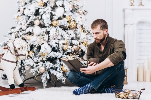 Livro de leitura de homem sênior perto da árvore de Natal decorada na véspera de xmas