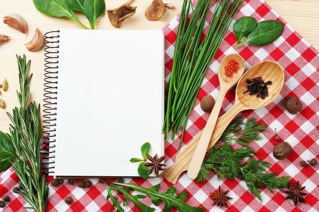 Livro de receitas aberto com ervas frescas e especiarias em fundo de madeira
