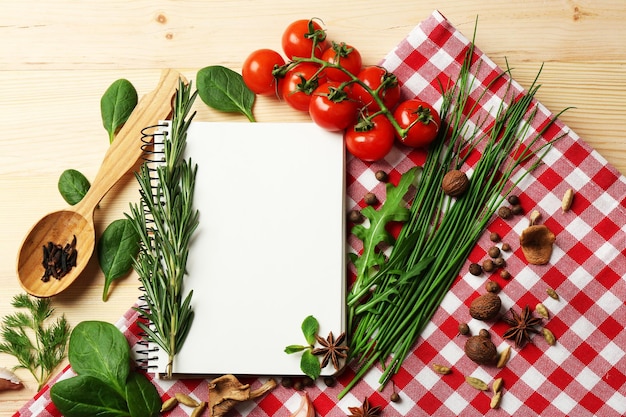 Livro de receitas aberto com tomates de ervas frescas e especiarias em fundo de madeira