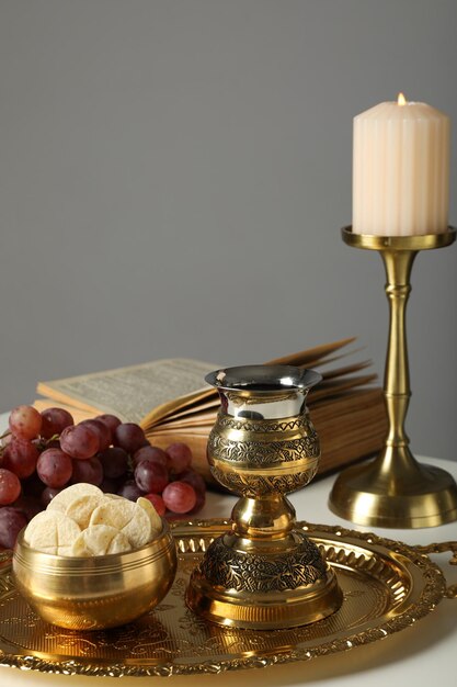 Livro de velas uvas pão litúrgico cruz dourada e copo na mesa em fundo cinza