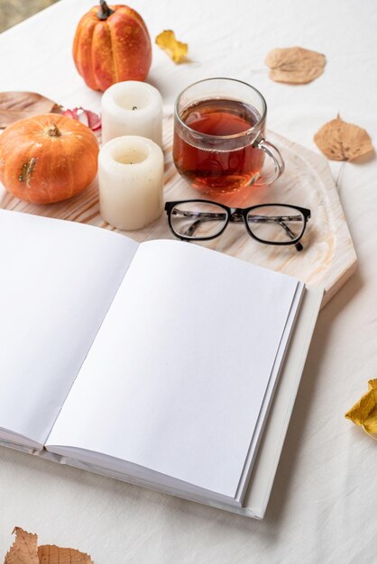 Livro em branco branco com óculos de folhas de outono e velas no design de maquete de mesa branca