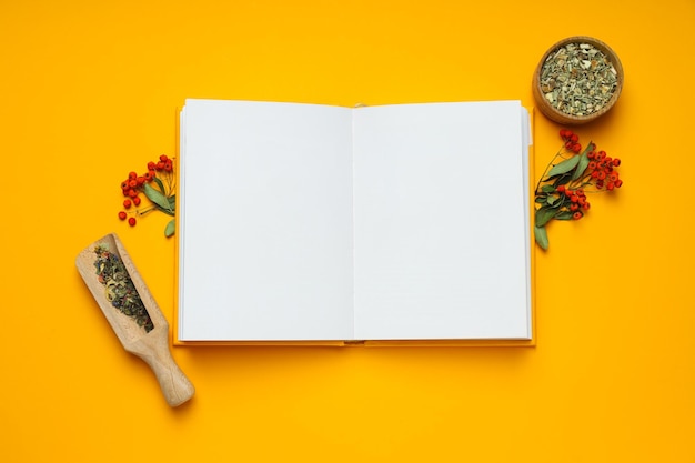 Livro em branco de medicina alternativa e ingredientes em fundo amarelo