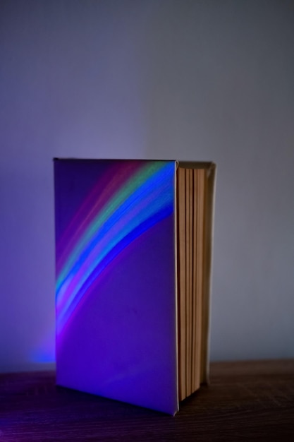 Livro mágico Conto de fadas noturno Fantasia imaginação Enciclopédia vintage para crianças com capa em branco na luz de neon do arco-íris no fundo do espaço de cópia da parede roxa iluminada escura