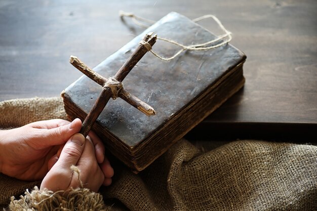 Livro religioso antigo e cruz de madeira no fundo de uma madeira e serapilheira