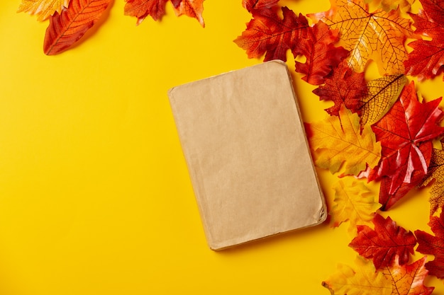 Livro romântico com folhas de outono em fundo amarelo. Vista do topo