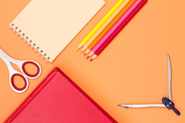 Livro, tesoura, caderno, lápis de cor e bússola no fundo rosa. Vista do topo. De volta ao conceito de escola. Material escolar. Cores pastel