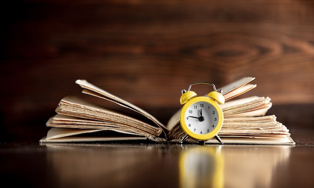 Livro velho e pequeno despertador na mesa de madeira