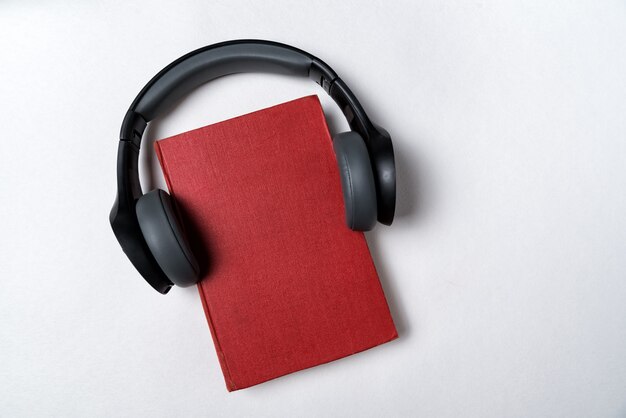 Livro vermelho com fones de ouvido em um fundo branco. Aprendendo com o conceito de áudio. Copie o espaço