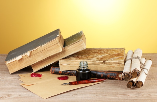 Livros antigos, pergaminhos, caneta e tinteiro na mesa de madeira sobre fundo amarelo