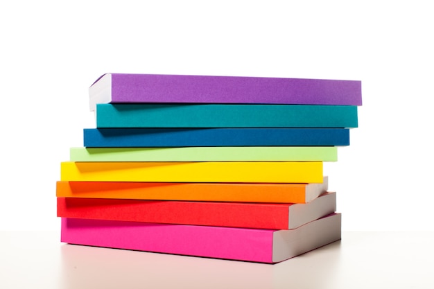 Foto livros coloridos são delineados com as cores do arco-íris. os livros empilhados em uma prateleira perto da parede branca