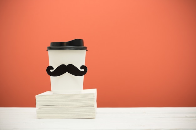 Foto livros e copo com bigode na mesa de madeira sobre fundo laranja. estilo hipster.