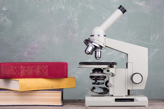 Livros e microscópio na mesa sobre fundo verde