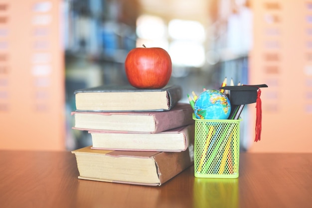 Livros na mesa na biblioteca Educação aprendendo pilha de livros antigos e boné de graduação em uma caixa de lápis com modelo de globo terrestre em mesa de madeira e estante de livros desfocado fundo da sala com maçã no livro