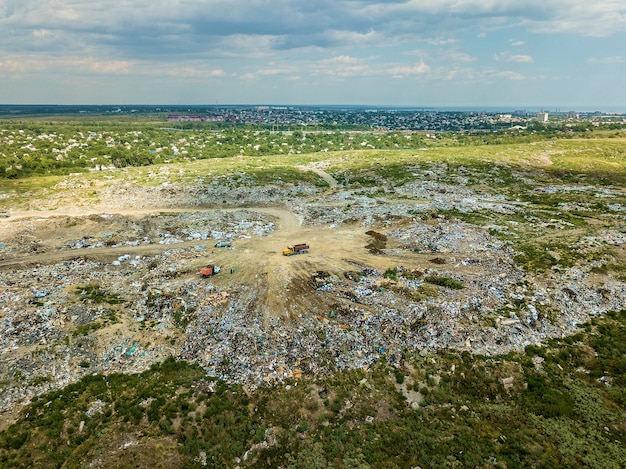 Lixeira na periferia da cidade perto de casas amarelas a escavadeira se move ao longo do aterro sanitário