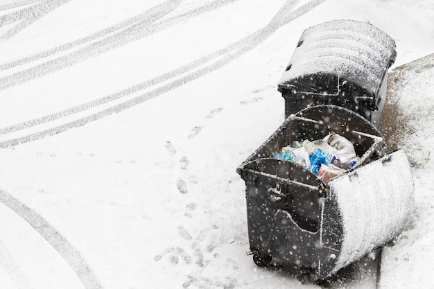 Lixeira quebrada coberta de neve. Pegadas e vestígios de carros na neve perto dos contêineres. Economia municipal