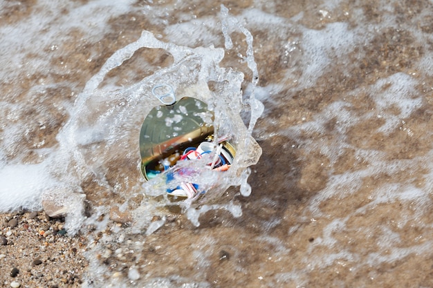 Lixo de plástico e lata foram arrastados pela onda do mar. Foco seletivo. Poluição ambiental por resíduos plásticos descartáveis. Microplásticos no oceano mundial.