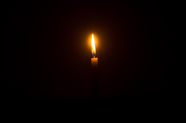 Llama de una sola vela encendida o luz que brilla en una vela naranja sobre fondo negro u oscuro en la mesa en la iglesia para el funeral de Navidad o el servicio conmemorativo