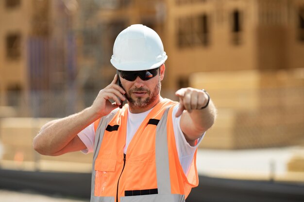 Llamada de constructor de trabajadores hispanos con teléfono en el sitio de construcción trabajador varón de mediana edad estadounidense mille