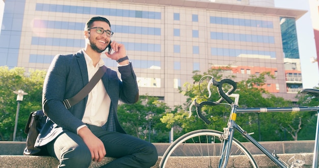 Llamada telefónica hombre de negocios y bicicleta en la ciudad para viajar con transporte ecológico Bicicleta celular y feliz profesional masculino hablando y discutiendo mientras está sentado en los escalones en la calle urbana