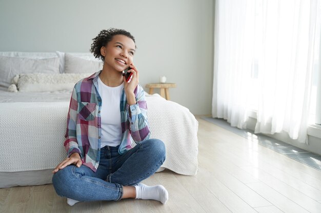 Llamada telefónica por la mañana Una adolescente con ropa informal está hablando con un amigo por teléfono inteligente en el dormitorio