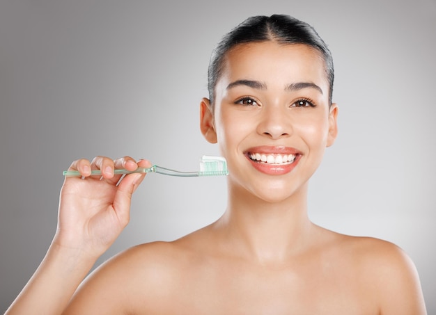 Llámalo seguro para tus dientes Foto de estudio de una atractiva joven cepillándose los dientes contra un fondo gris