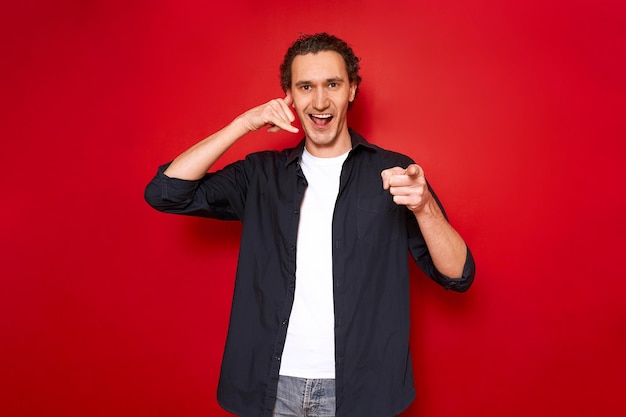 Llámame mano signo retrato de joven sonriente señalando con el dedo índice delante de representa teléfono