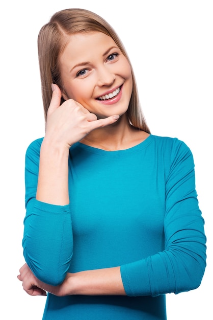 ¡Llámame! Mujeres jóvenes alegres gesticulando señal de teléfono y sonriendo mientras está de pie contra el fondo blanco.