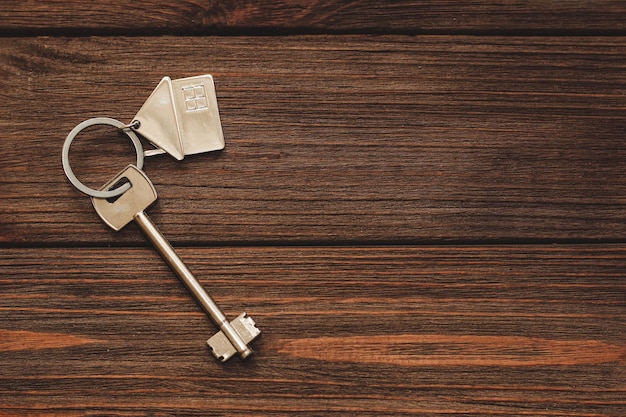 La llave del apartamento con un llavero en forma de casa sobre fondo de madera