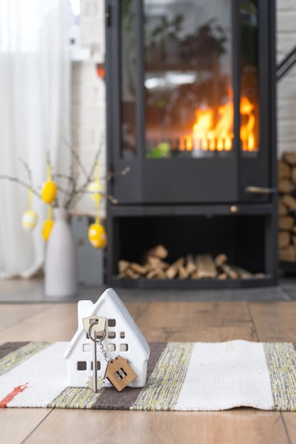 Llave de la casa cerca de la estufa de la chimenea con fuego y leña Acogedor hogar con decoración de pascua huevos coloridos en una canasta y conejito Edificio en movimiento hipoteca alquiler y compra seguro de bienes raíces