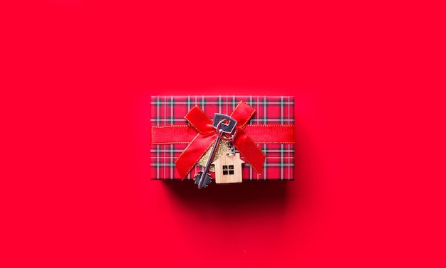 Llave de casa con llavero de cabaña. Feliz año nuevo fondo rojo, regalo, tarjeta de felicitación. Compra, construcción, reubicación, hipoteca