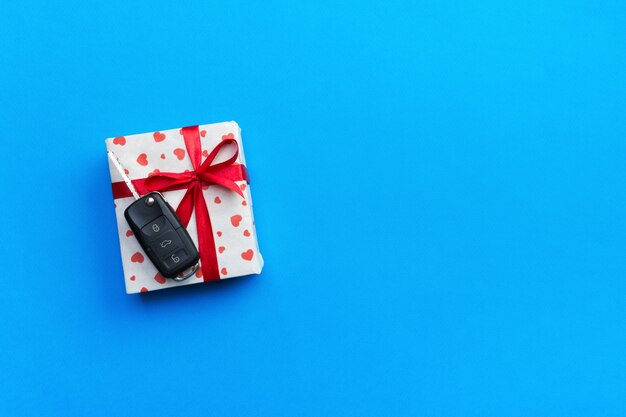 Llave del coche en la caja de regalo de papel con el arco y el corazón rojos de la cinta en la tabla azul. copyspace Vacaciones presente concepto vista superior