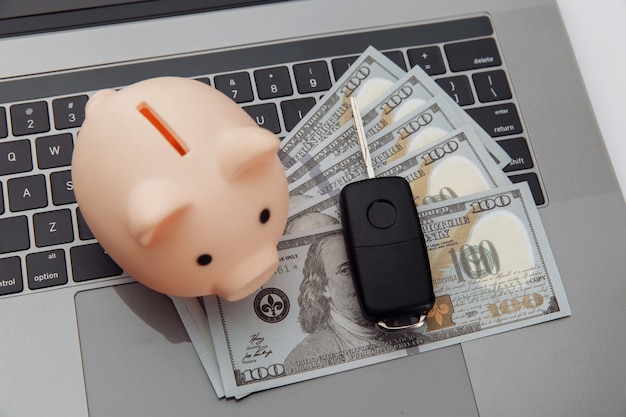 Foto llave del coche y hucha con dinero en una computadora portátil. concepto de coche de compra online.