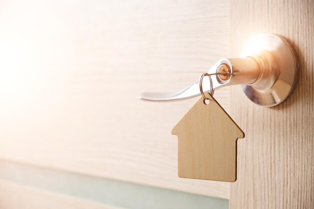 Llave con llavero en forma de casa en la cerradura de la puertaCon luz solar brillante