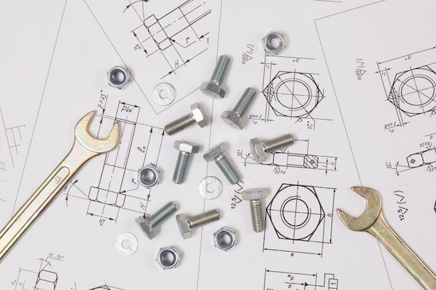 Llave, pernos y tuercas sobre dibujos de ingeniería.