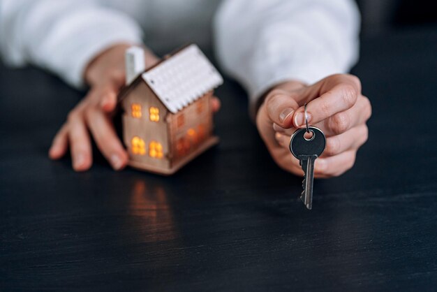 Llaves de la casa en manos de una mujer y una pequeña maqueta de una casa con ventanas luminosas cercanas. concepto de adquirir tu vivienda