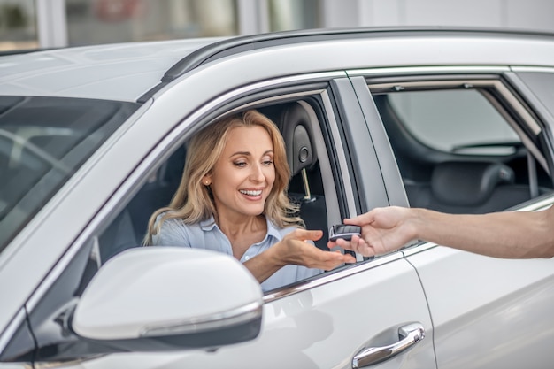 Llaves del coche. Sonriente mujer rubia tomando las llaves del coche y mirando contento