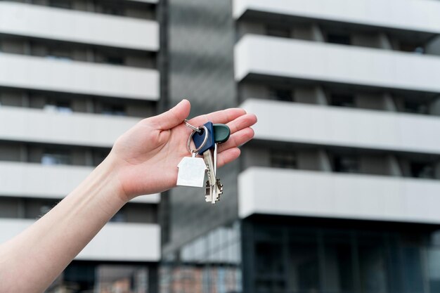 Llaves con un llavero en una mano femenina frente a la casa de apartamentos