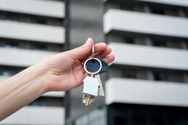 Foto llaves con un llavero en una mano femenina frente a la casa de apartamentos