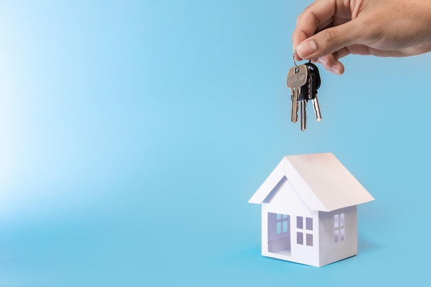 Llaves de mano y modelo de casa blanca en fondo azul para el plan de refinanciamiento y el concepto de bienes raíces.