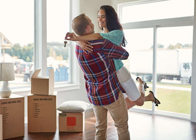 Foto llaves de pareja felices y mudarse a un nuevo hogar o abrazo por hipoteca o compra de propiedad y cajas en un salón vacío juntos hombre y mujer de bienes raíces emocionados por alquilar o abrazar y casa con espacio abierto