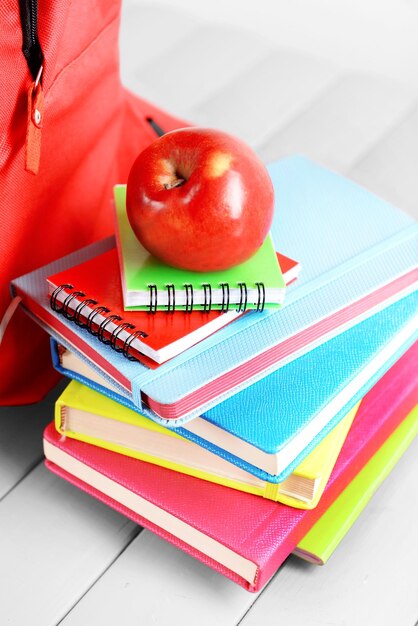 Foto llena de mochila roja estacionaria y pila de libros con manzana en la parte superior en la mesa de madera de cerca