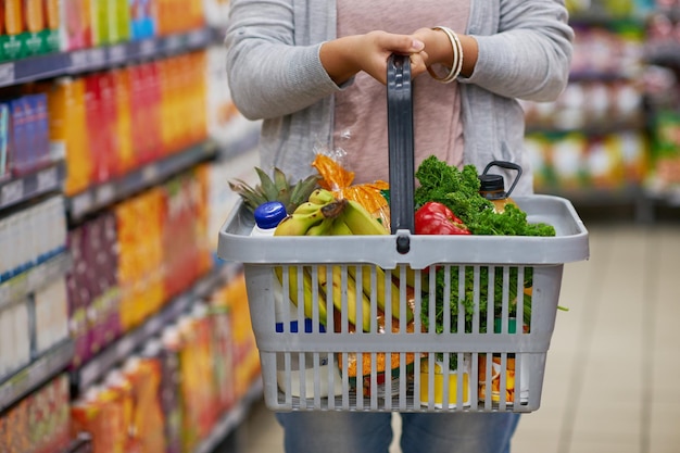 Llenándose de algo de frescura Primer plano de una mujer sosteniendo una cesta llena de comestibles en un supermercado