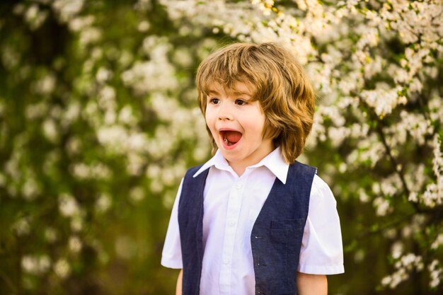 Lleno de alegría, el niño feliz tiene un cabello exuberante y saludable. Moda de verano y primavera. El niño disfruta de la naturaleza floreciente en parte.