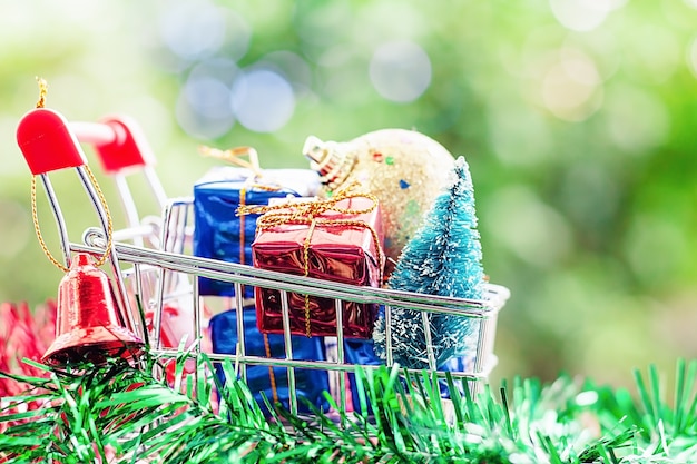 Lleno de artículos decorativos de Navidad en mini carrito de compras contra backgrou verde natural borroso