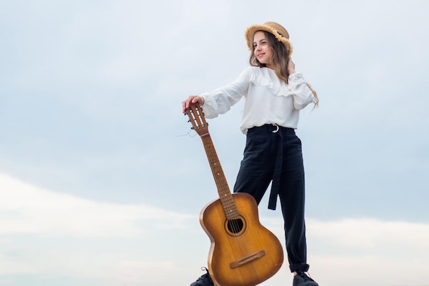 Lleno de inspiración libertad y éxito cantante feliz adolescente niña tocando la guitarra al aire libre infancia feliz niño bonito en el cielo fondo música country concepto niño moda estilo copia espacio